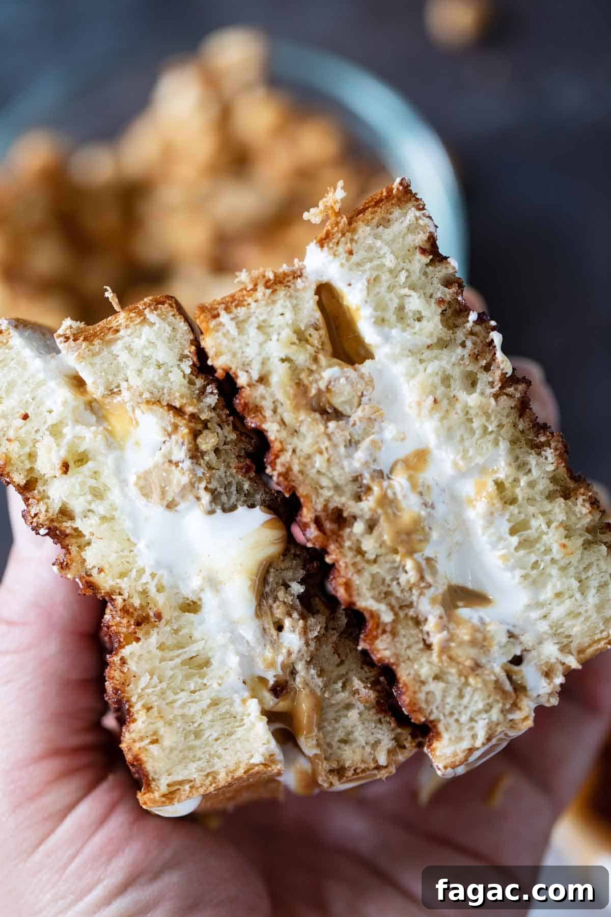 A version of a New England classic, this Fluffernutter Panini has melted marshmallow creme, peanut butter and candied peanuts all toasted on cinnamon sugar crusted bread. Hands holding a fluffernutter that is cut in half to show inside.
