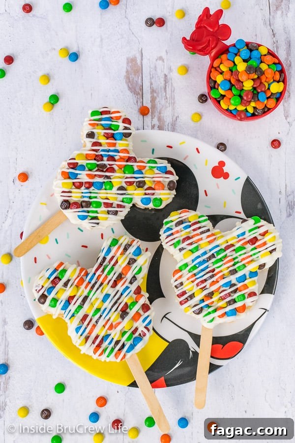 M&M's Mickey Mouse Rice Krispie Treats - these Mickey shaped treats are one of the easiest Disney copycat recipes. Easy treat to make for the Disney fan in your life. An overhead picture of three M&M's Mickey Mouse Rice Krispie Treats on a Mickey Mouse plate with M&M's scattered around