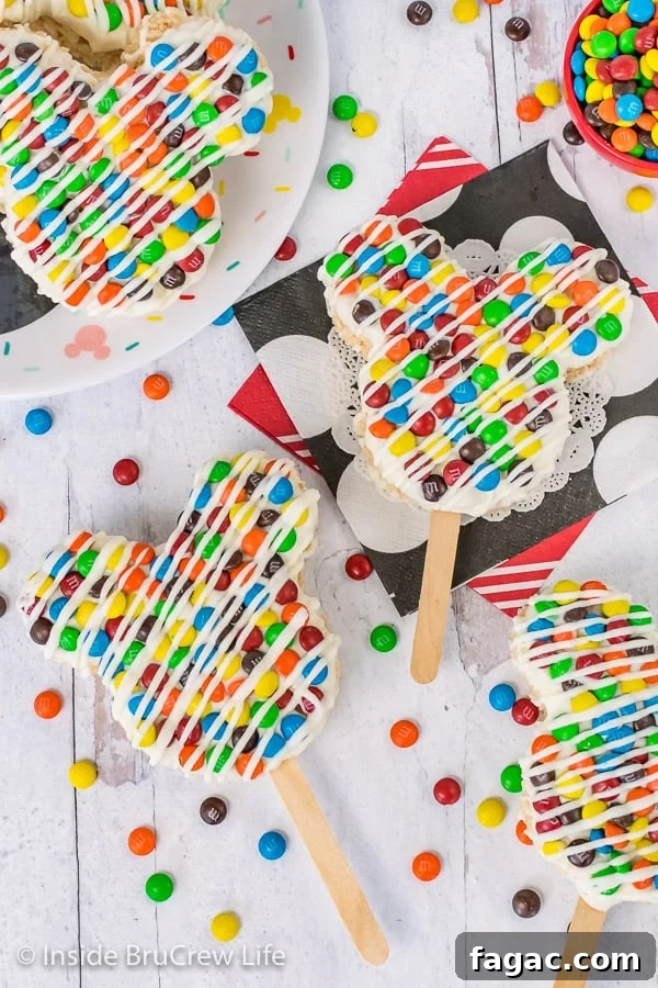 M&M's Mickey Mouse Rice Krispie Treats - candy and chocolate makes these rice krispie treats look just like the Mickey treats in the Disney parks. Overhead picture of M&M's Mickey Mouse Rice Krispie Treats on a white background with M&M's scattered around them