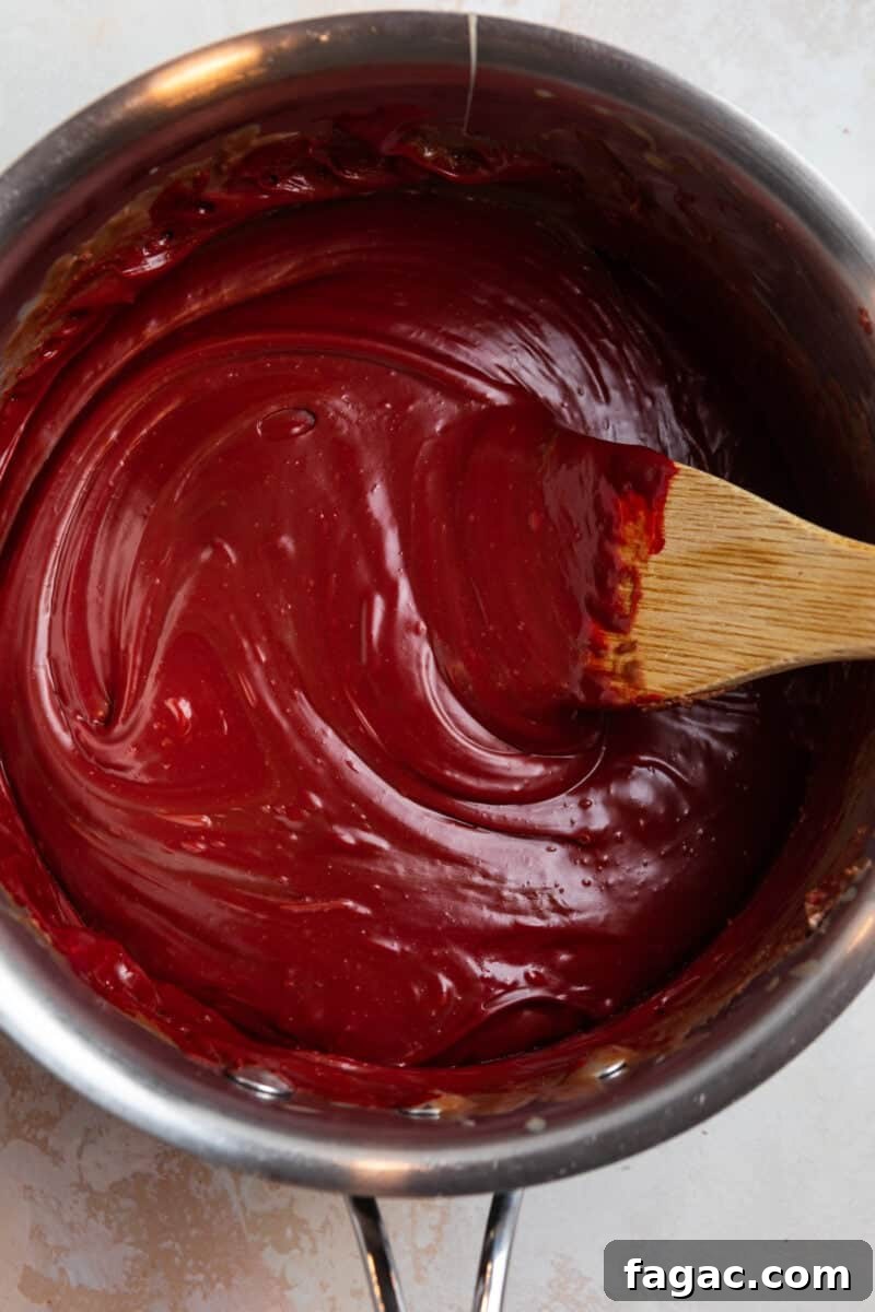Decadent Red Velvet Oreo Fudge Recipe for Dessert Lovers 6 Red velvet fuge prepped in sauce pan with wooden spoon.