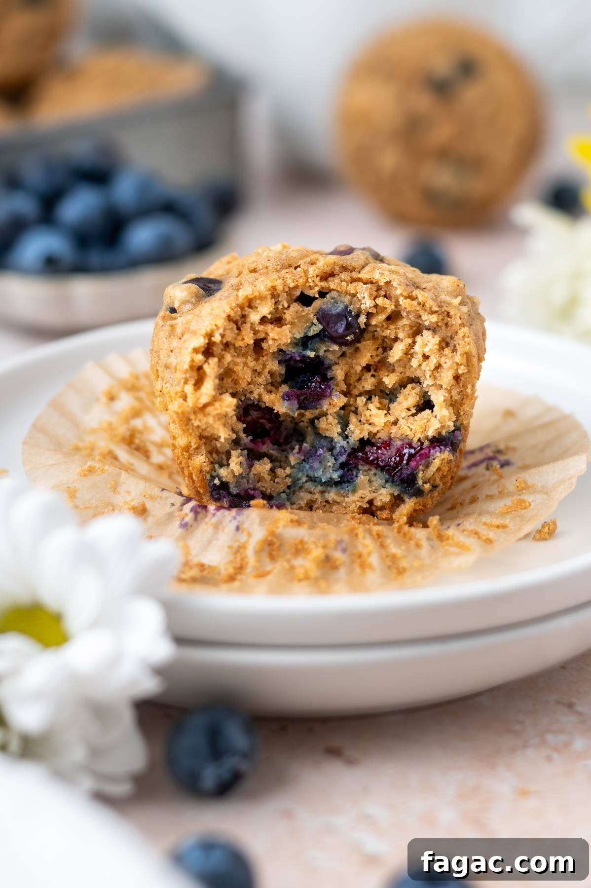 muffin on a plate showing soft and moist interior with a bowl of blueberries and more muffins in the background