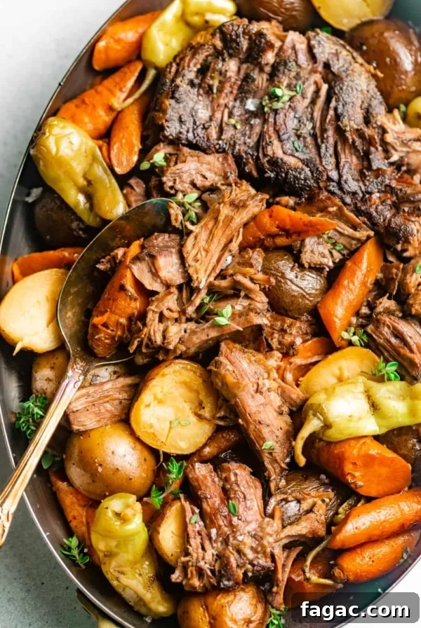 mississippi pot roast in a serving dish with a spoon and garnished with fresh thyme and pepperoncini peppers.