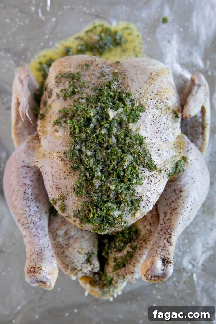 Crispy Roast Chicken with Herb Butter and Lemon 5 Raw chicken on a large baking sheet covered seasoned with salt and pepper and covered with butter, garlic, and fresh minced herbs.