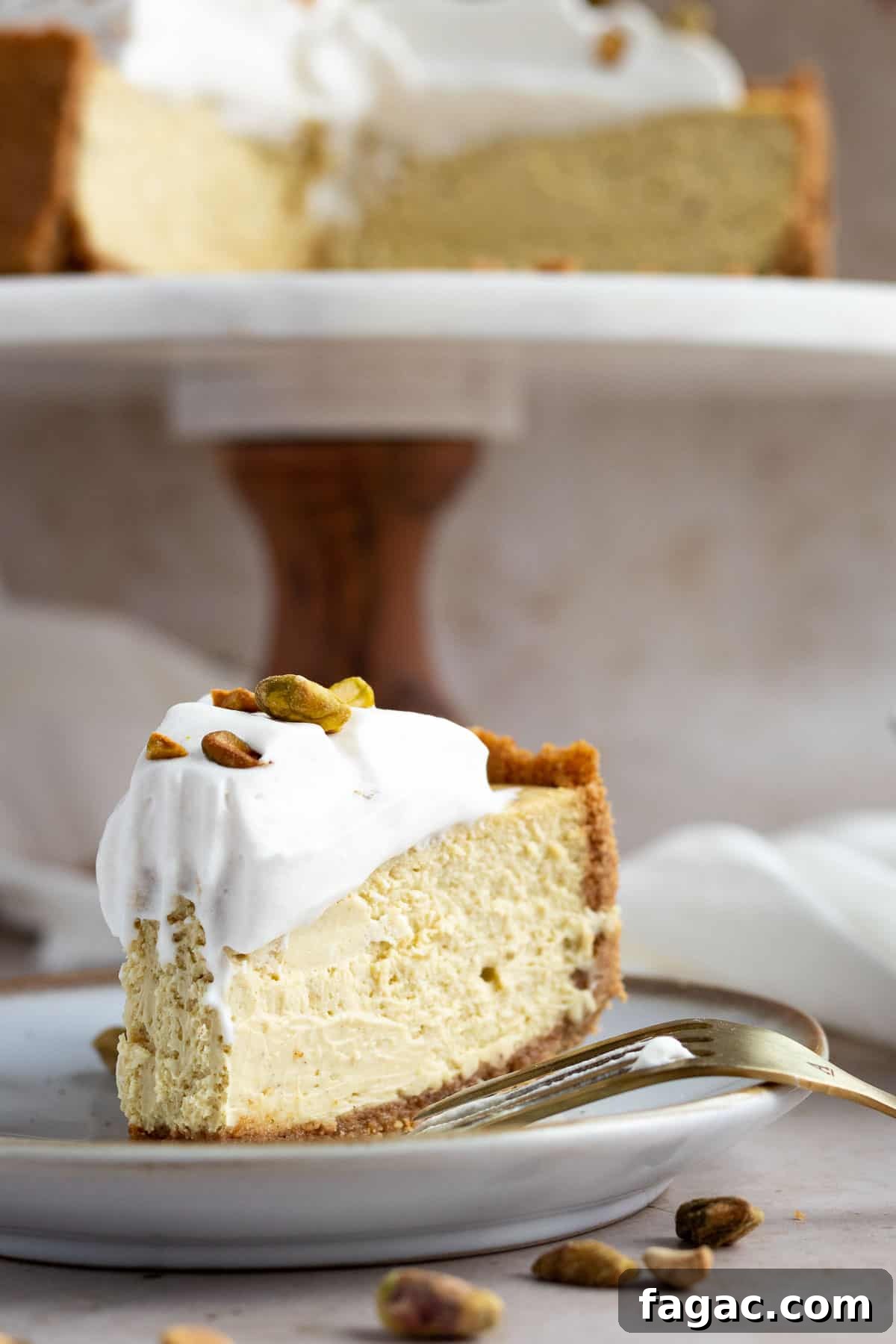 Brown Butter Graham Crust Pistachio Cheesecake Recipe 4 pistachio cheesecake slice on a plate with the whole cheesecake on a cake stand behind it