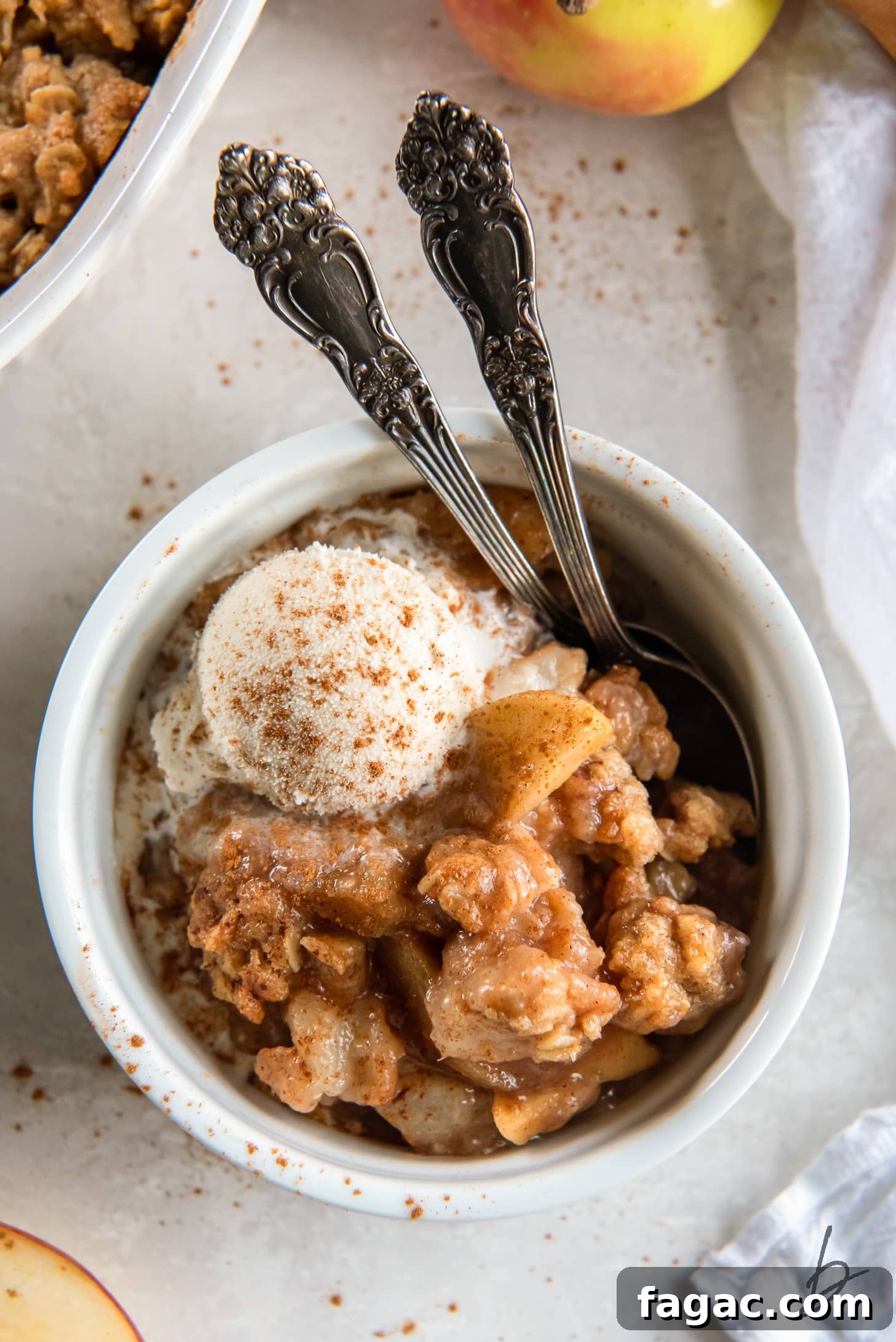 Ina Garten-Style Apple Pear Crisp Recipe 2 serving of apple pear crisp in a large ramekin with scoop of ice cream and two spoons.