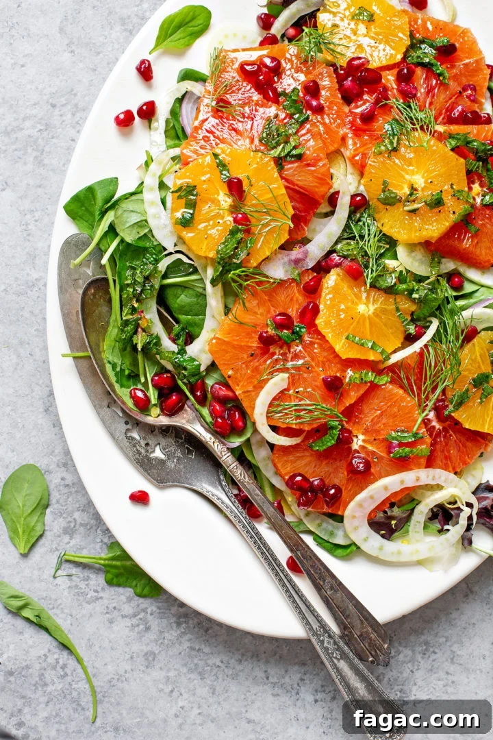fennel salad with oranges and pomegranate on a white platter with serving utensils