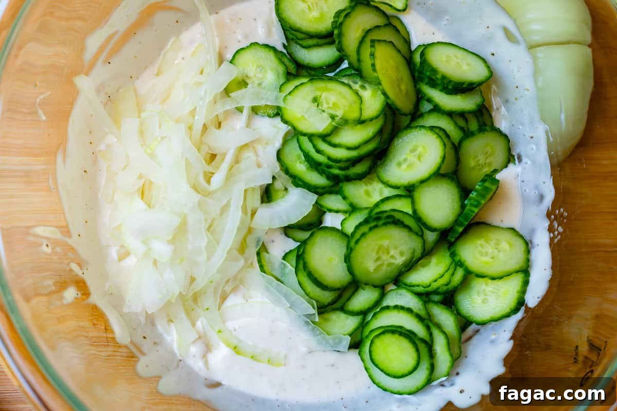 Aunt Joy’s Creamy Cucumber Salad Recipe for Summer Sides 11 Clear glass bowl with sliced English cucumbers, onions, cream, and spices.