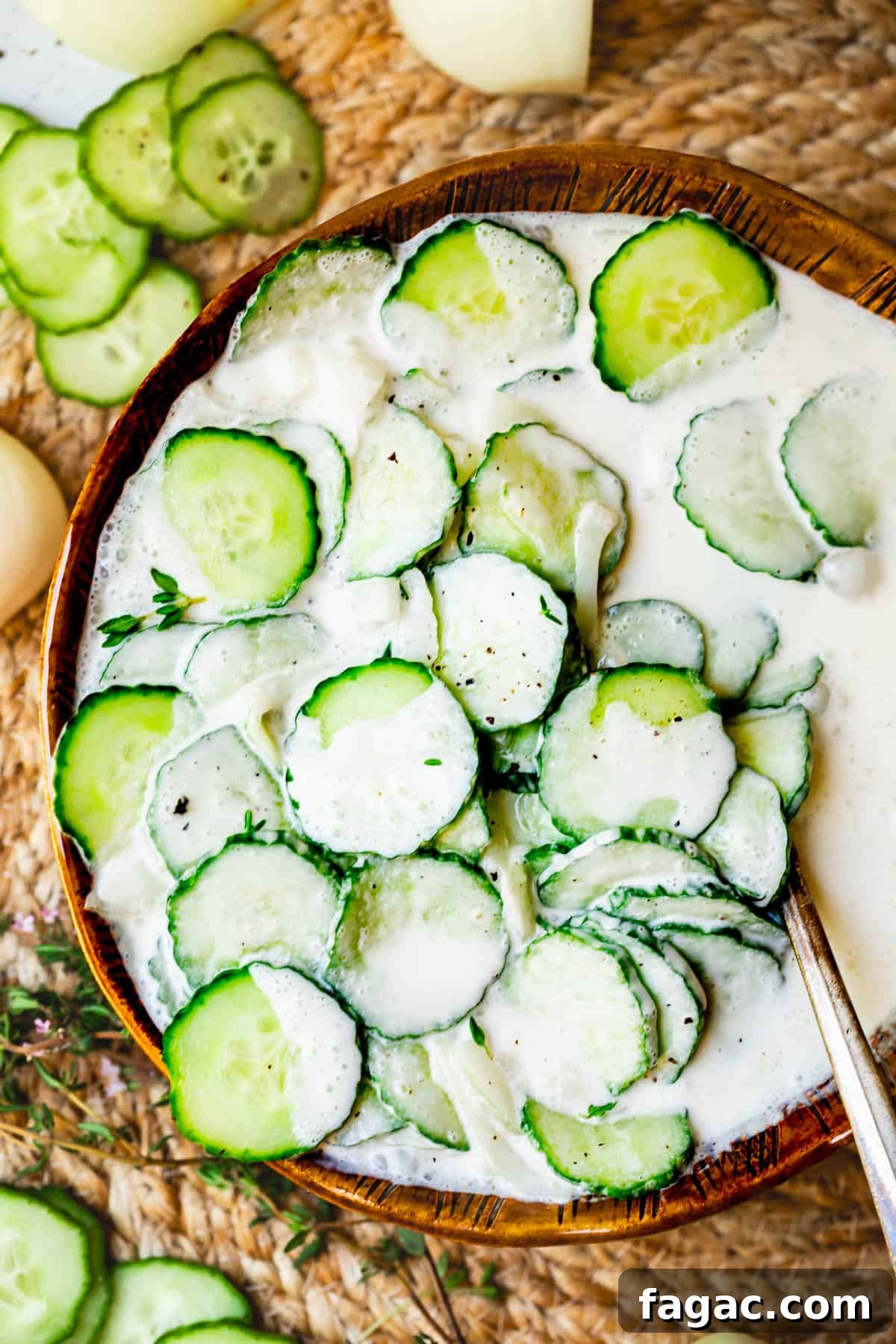 Aunt Joy’s Creamy Cucumber Salad Recipe for Summer Sides 14 creamy cucumber salad in a brown clay bowl with onions and thyme, on a woven placemat.