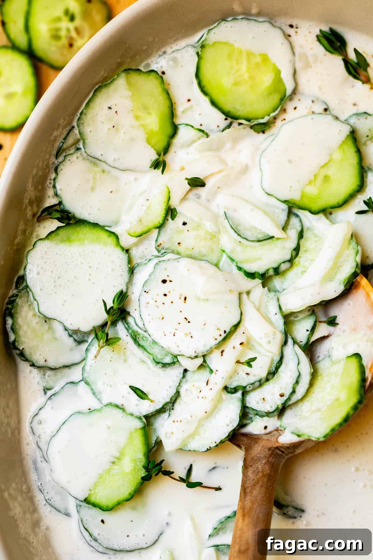 Aunt Joy’s Creamy Cucumber Salad Recipe for Summer Sides 16 creamy cucumber salad with onions and thyme in a white bowl with wooden spoon.