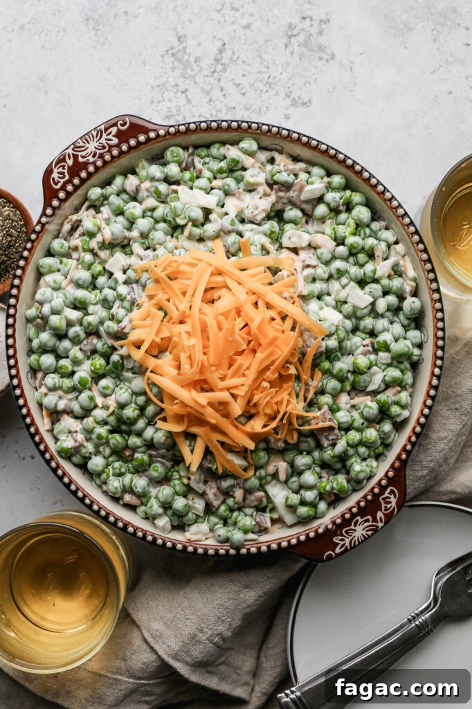 a bowl of easy pea salad with shredded cheddar cheese sprinkled on top next to a little wooden bowl of pepper and a little ceramic bowl of salt