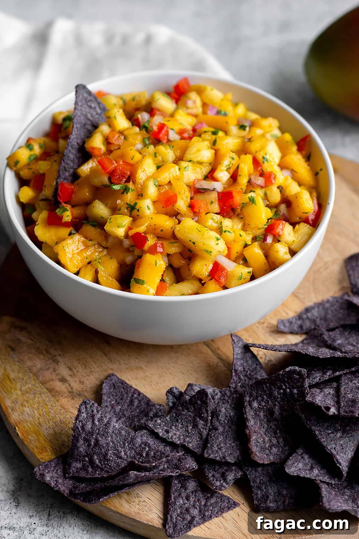 Zesty Mango and Pineapple Salsa Recipe for Summer Parties 2 White bowl with diced mangos, pineapples and blue corn tortilla chips.