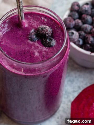 Glass cup with a purple smoothie, metal straw and frozen blueberries.