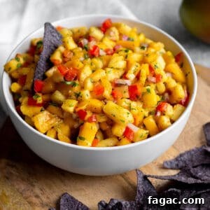 Zesty Mango and Pineapple Salsa Recipe for Summer Parties 10 A bowl with diced mangos, pineapples and blue corn tortilla chips on a wooden board.