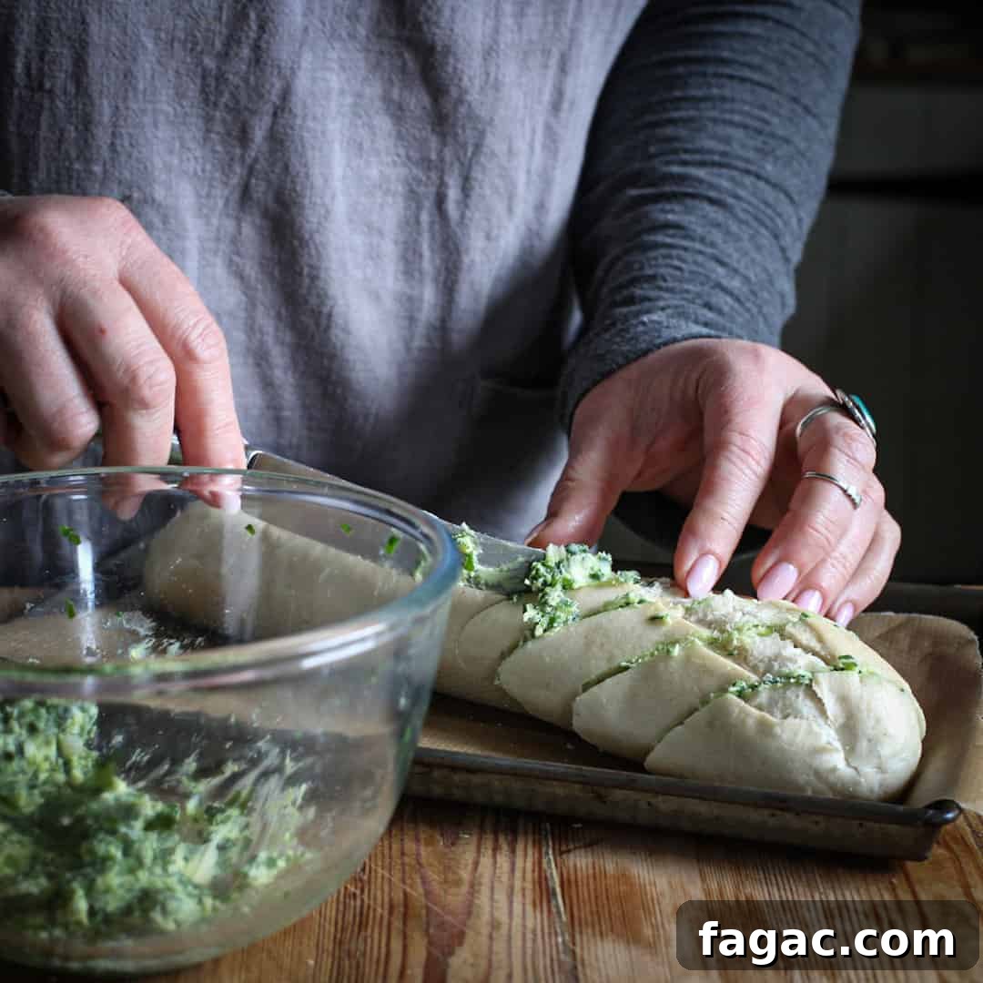 Crispy Wild Garlic Bread Recipe for Spring Gatherings 9 Womans hands spreading bright green wild garlic butter onto a part baked baguette