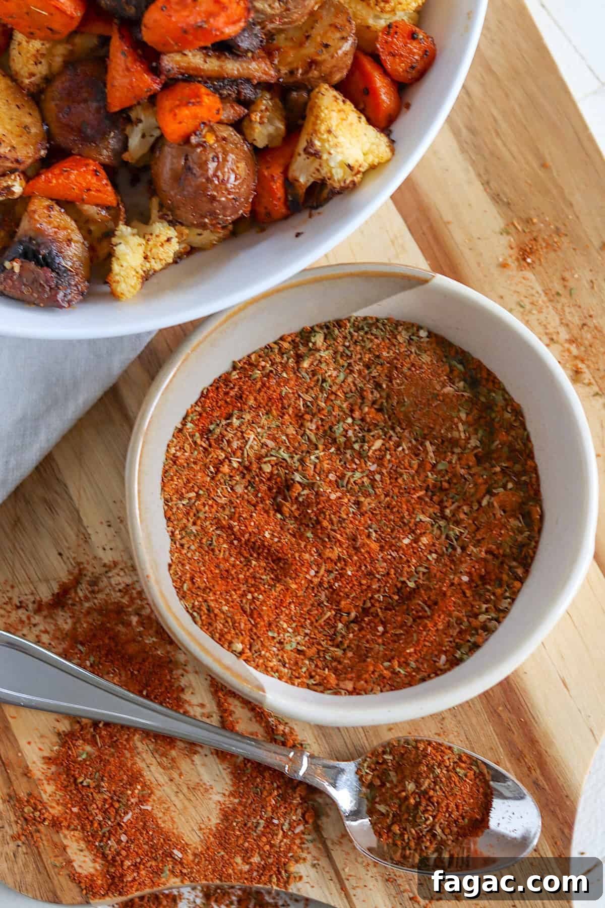 A white bowl of roasted vegetable seasoning mix with a spoon on a wooden board.