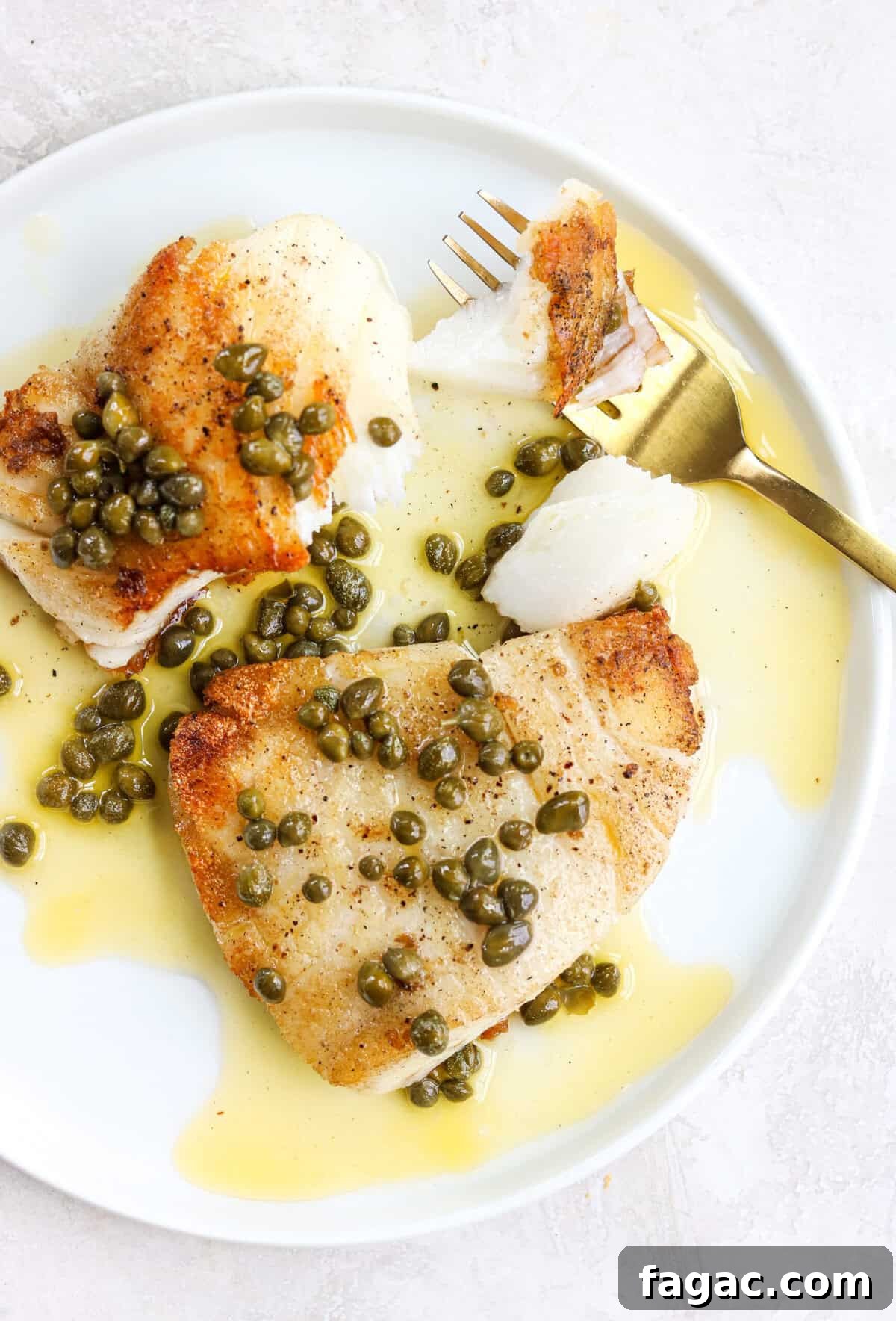 crispy pan seared white fish on a white plate with lemon caper sauce and a gold fork with a bit of fish on it