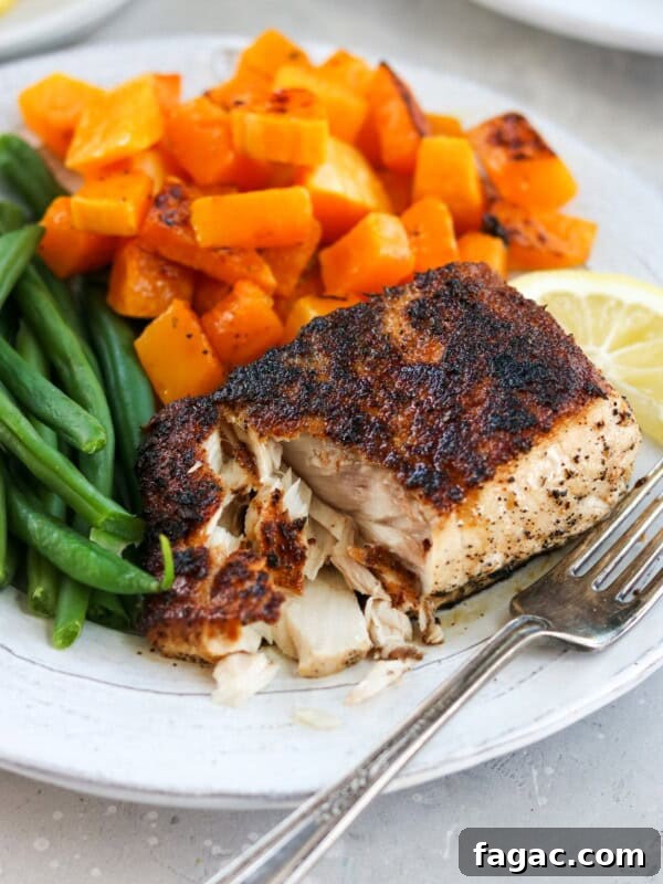blackened mahi mahi on a plate with butternut squash and green beans with a fork flaking the fish apart