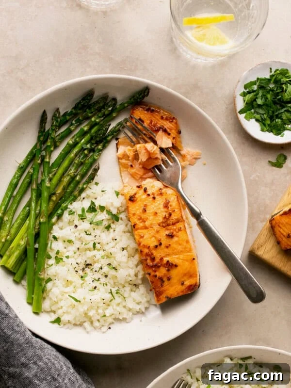 air fryer frozen salmon with honey garlic sauce and cauliflower rice and asparagus in a bowl with a fork flaking the fish