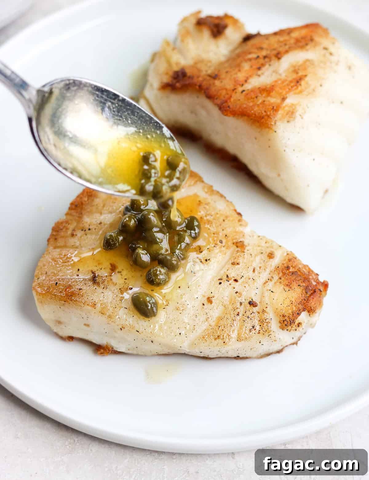 a silver spoon drizzling lemon caper butter over a piece of Chilean sea bass on a white plate