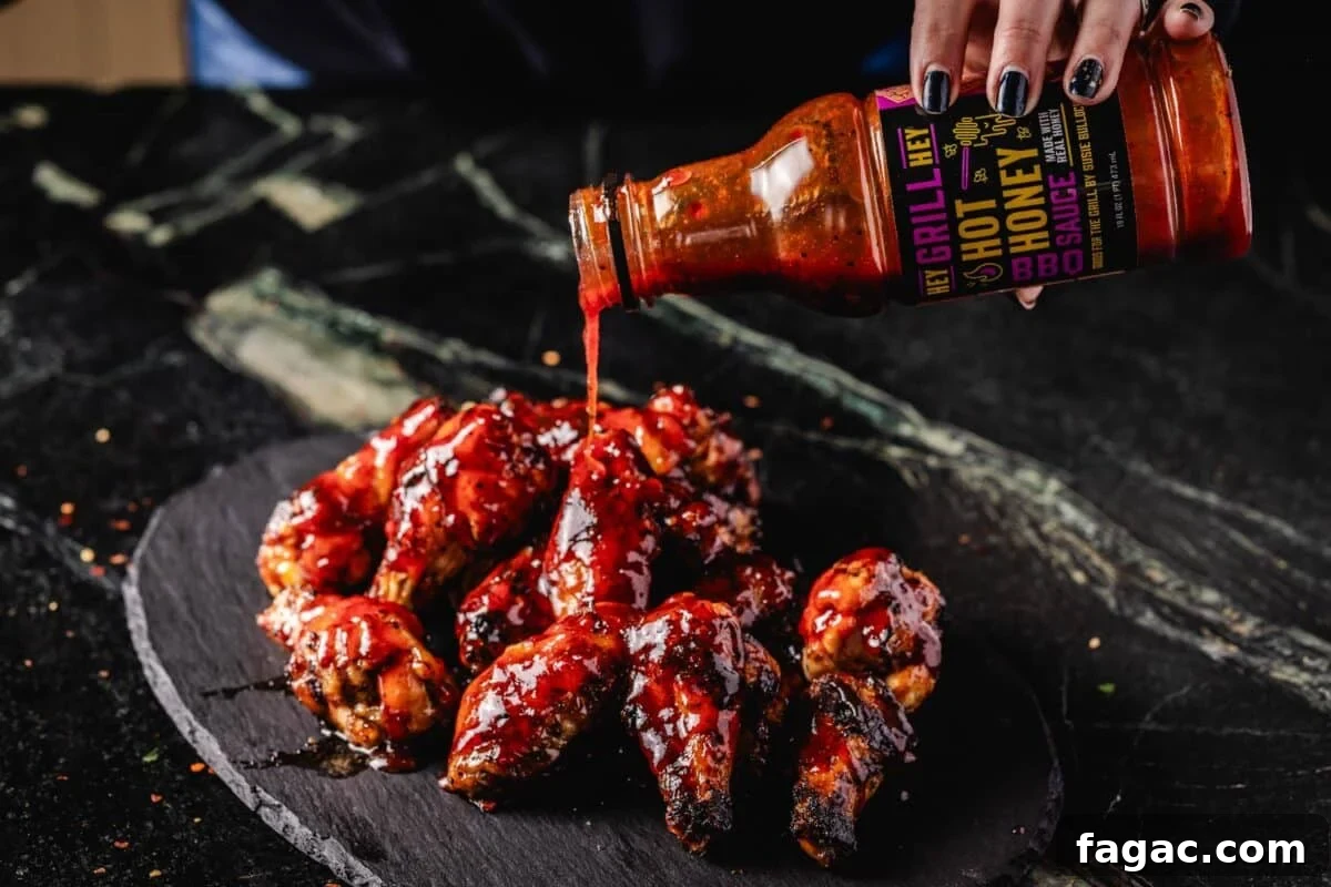 Spicy Honey BBQ Sauce Recipes for Grilling and Glazing 7 A pile of wings on a black platter and a bottle of sauce pouring onto them.