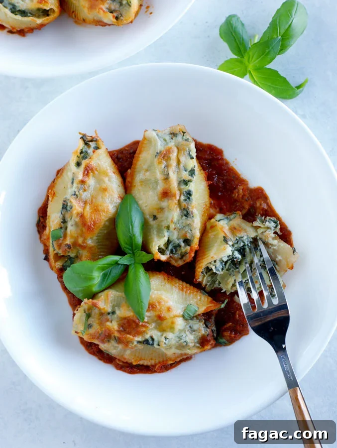 Spinach and Artichoke Stuffed Pasta Shells for Dinner 2 A white bowl with 4 spinach artichoke stuffed shells with a fork and some fresh basil.