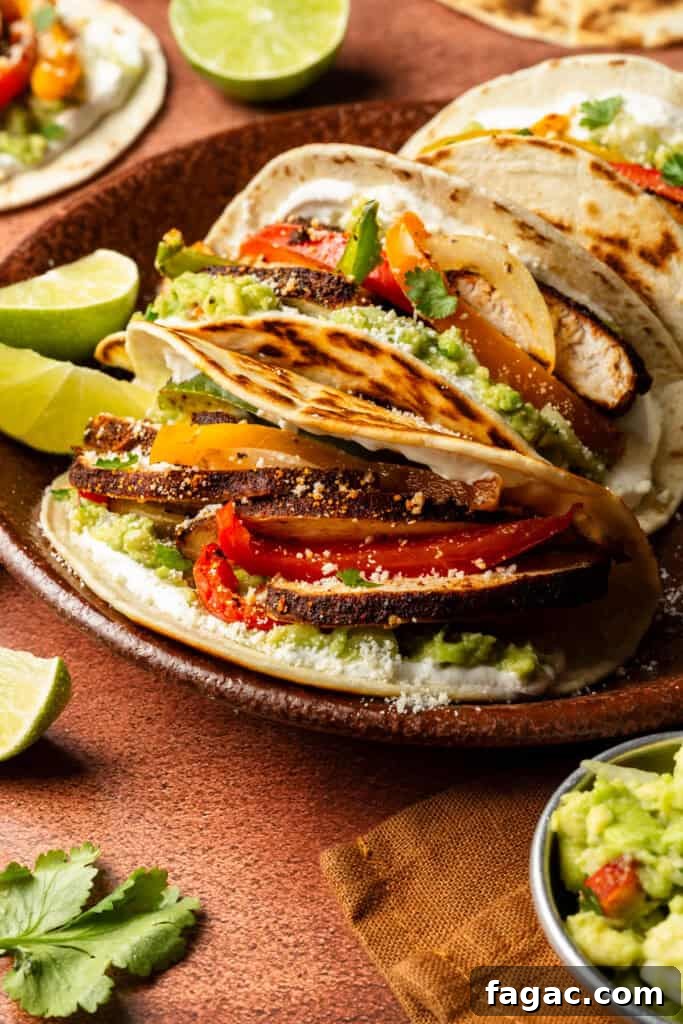 Weeknight Sheet Pan Chicken Fajitas Recipe for Quick Dinners 11 A 3/4 angle view of the inside of an assembled fajita. The tortilla has guacamole, cotija cheese, roasted peppers, onions, and chicken breast slices.