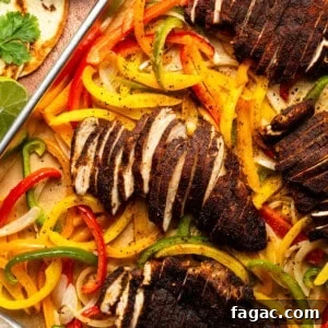A bird's eye view of a pan of roasted peppers and onions, topped with seasoned, sliced chicken breast. Fajita toppings surround the pan.