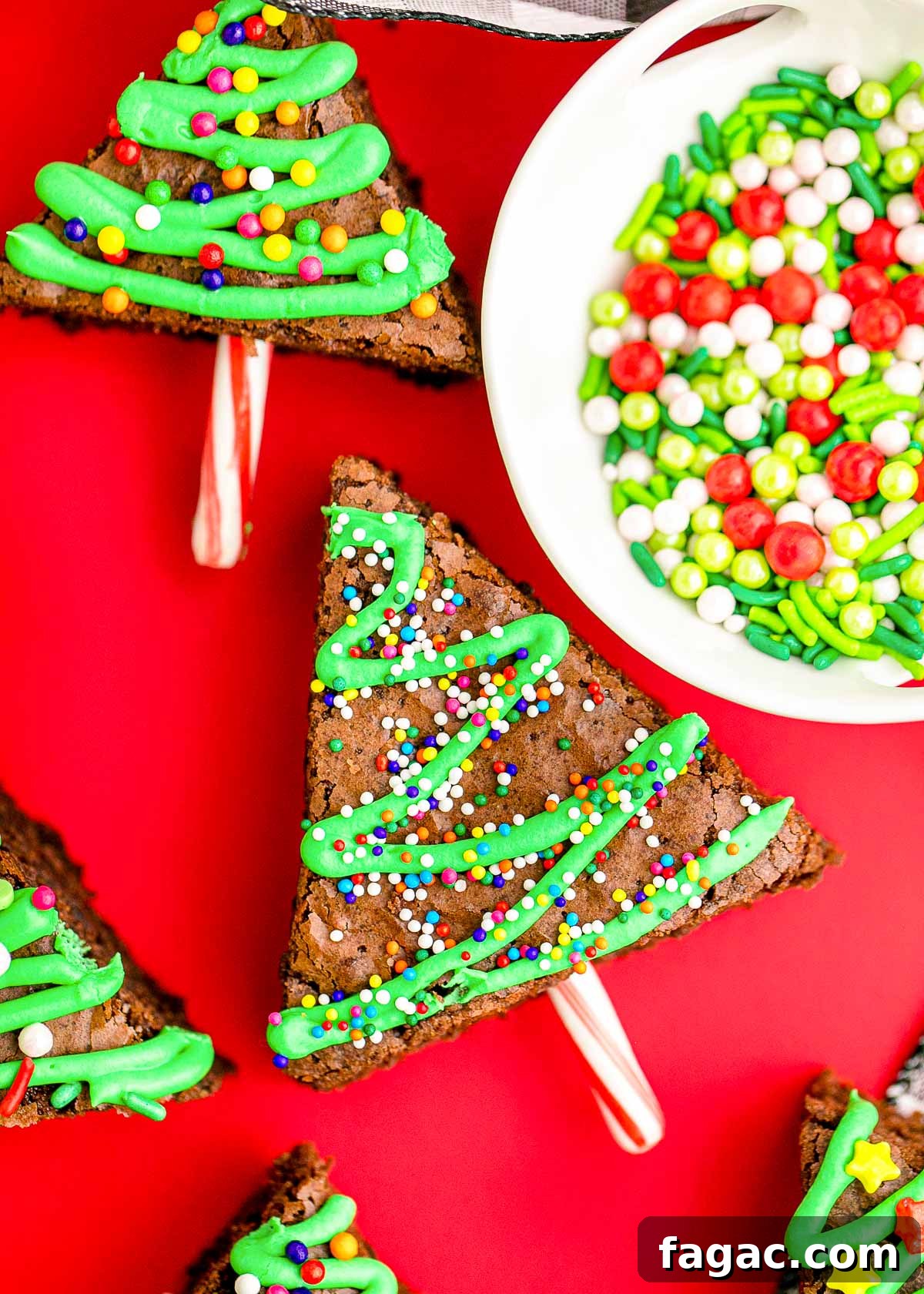 Close up photo of brownie christmas trees laying on a red surface with a bowl of sprinkles next to them.