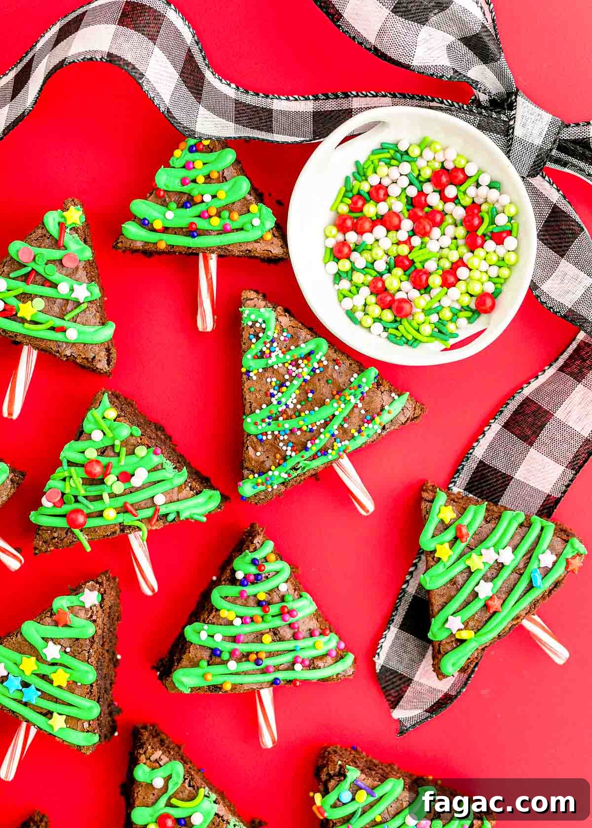 Overhead photo of brownie Chrsitmas trees on a red surface with holiday ribbon and sprinkles around them.