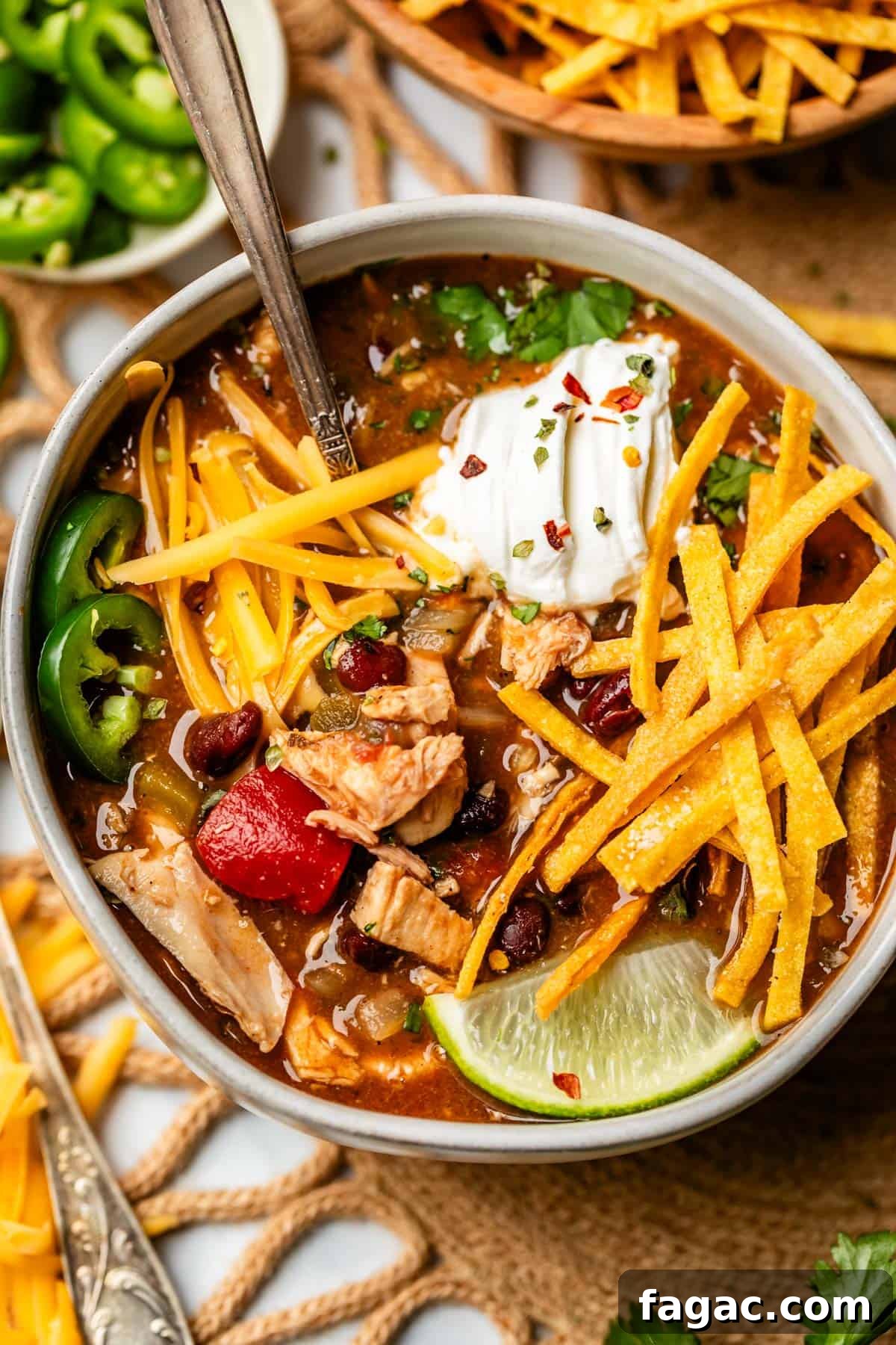 Quick Chicken Tortilla Soup Recipe for Cozy Weeknight Meals 21 ceramic bowl filled to the brim with soup and toppings like tortilla strips and cheese.