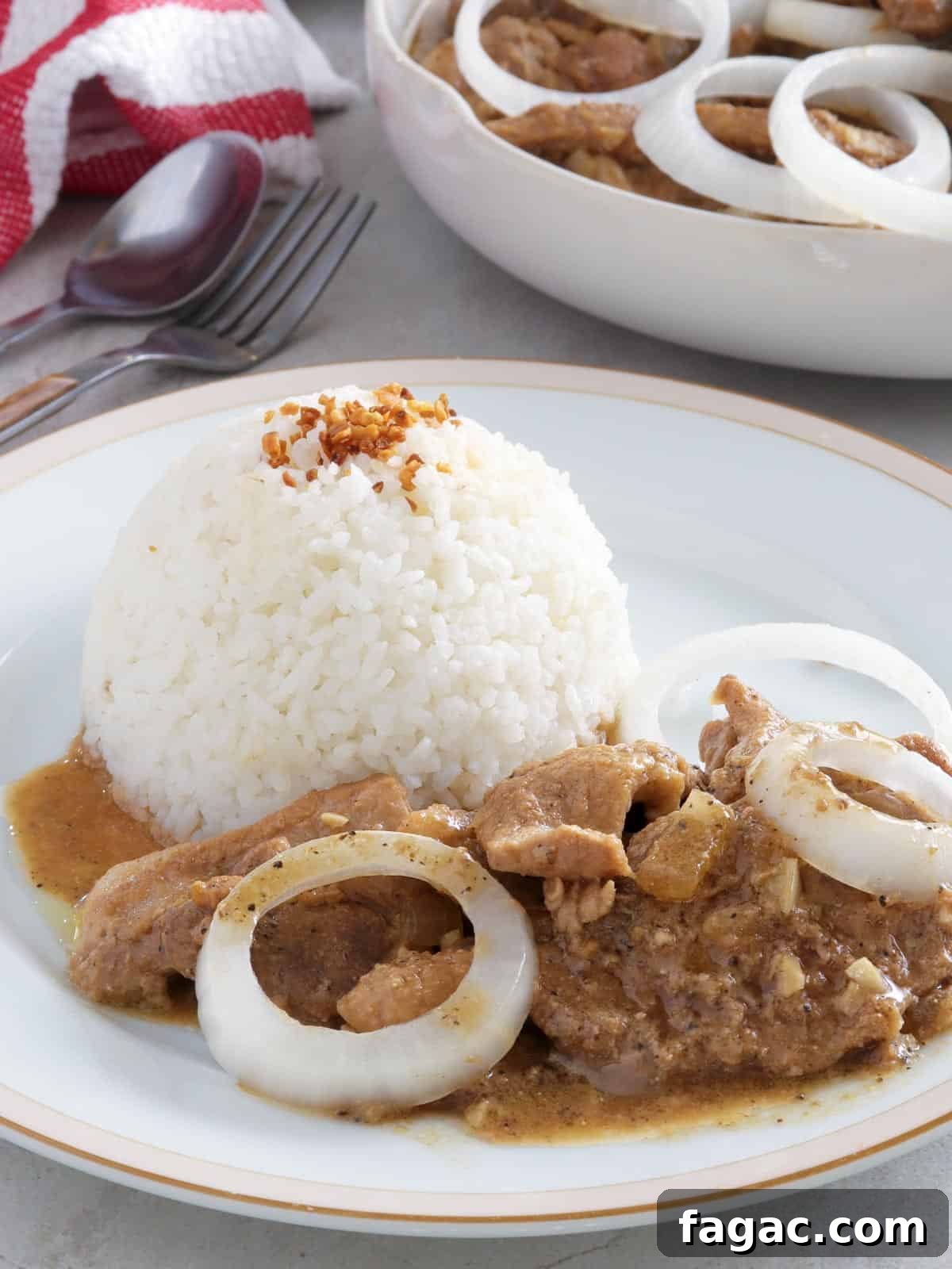 Creamy pork bistek on a white plate with steamed rice on the side.