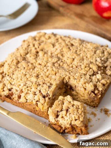Applesauce crumb cake with a slice taken out on a white plate.
