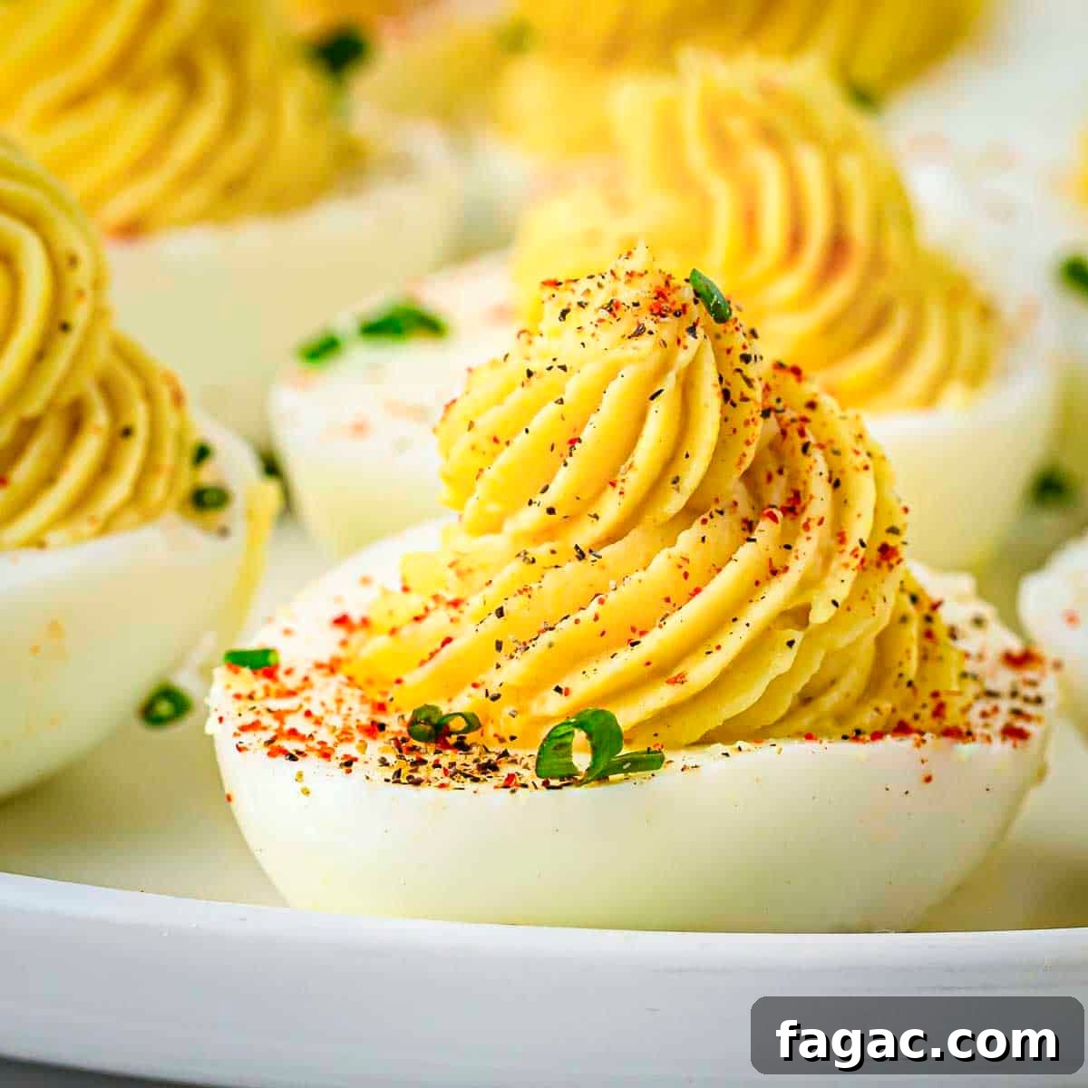 Side shot of multiple deviled eggs garnished with paprika and chives on a white plate.