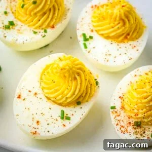 Overhead close up shot of multiple deviled eggs garnished with paprika and chives on a white plate.
