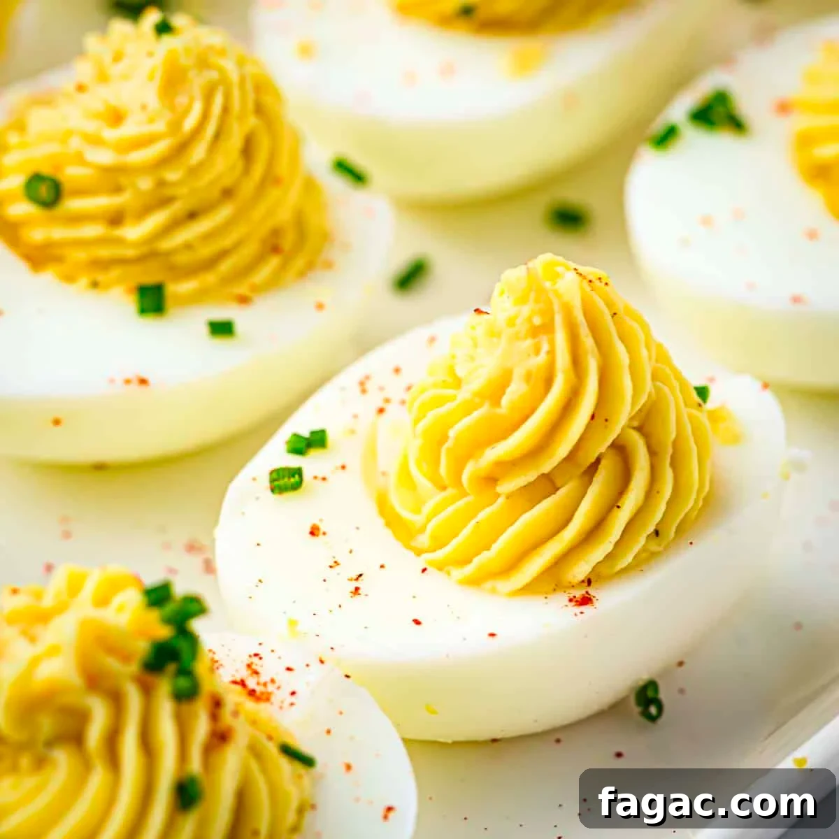 Side close up shot of multiple deviled eggs garnished with paprika and chives on a white plate.
