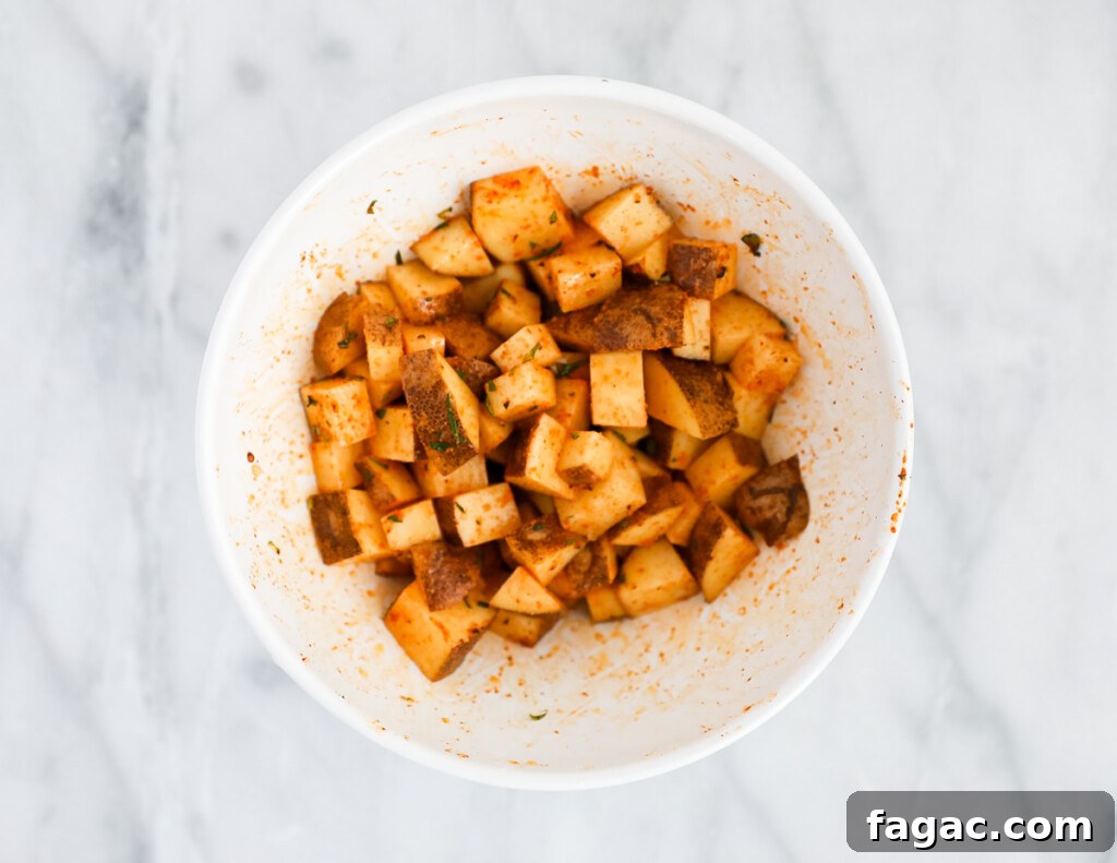 A large white bowl filled with uncooked diced potatoes covered in seasoning