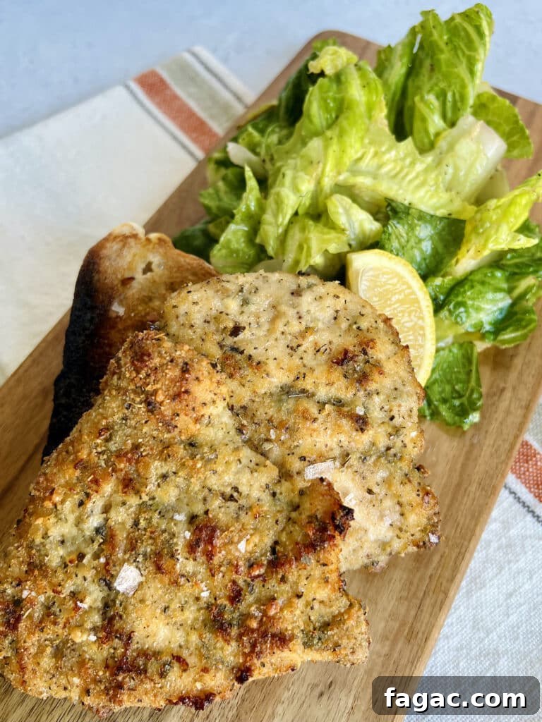 Crispy baked chicken cutlets sprinkled with sea salt and serving board with green salad and lemon wedge.