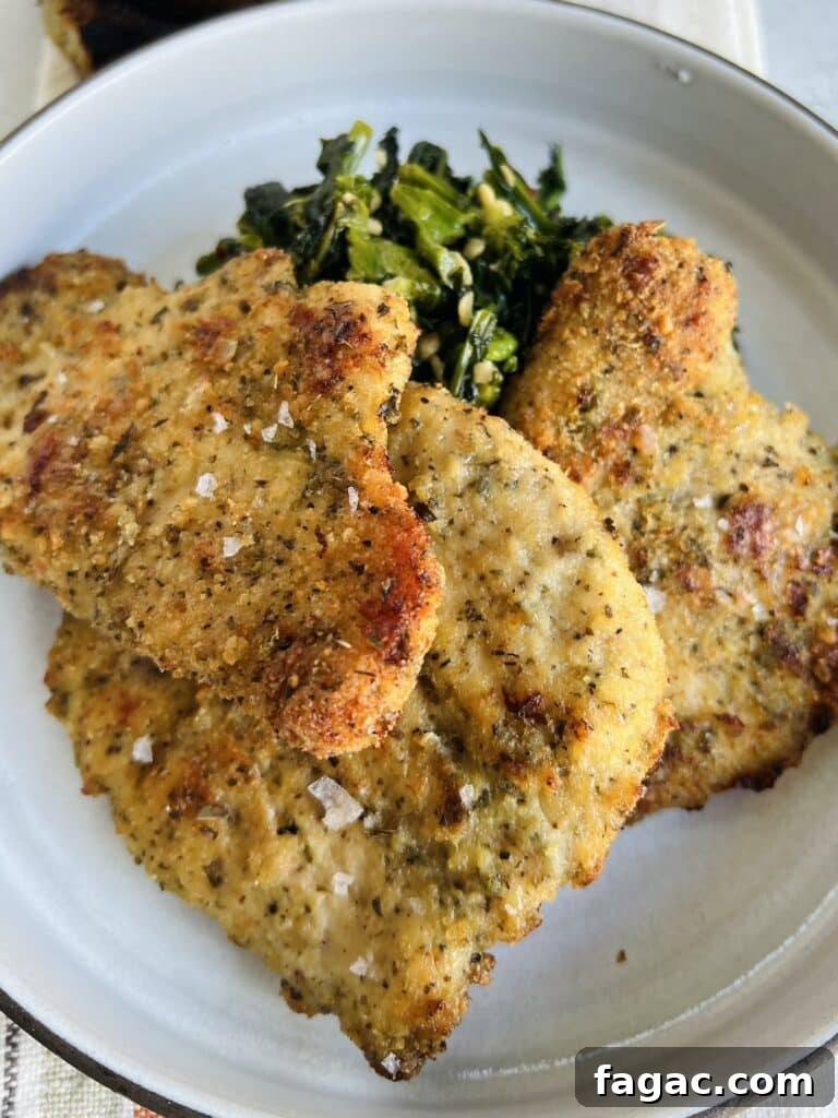 Baked chicken cutlets, Italian style, on plate with sautéed broccoli rabe.