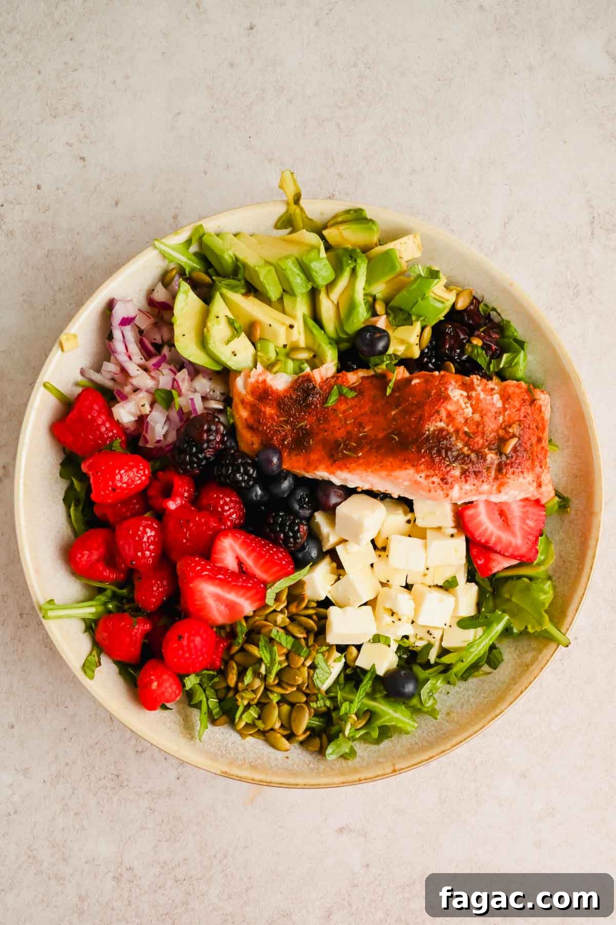 salad with berries, avocado, cheese and pumpkin seeds topped with broiled salmon.