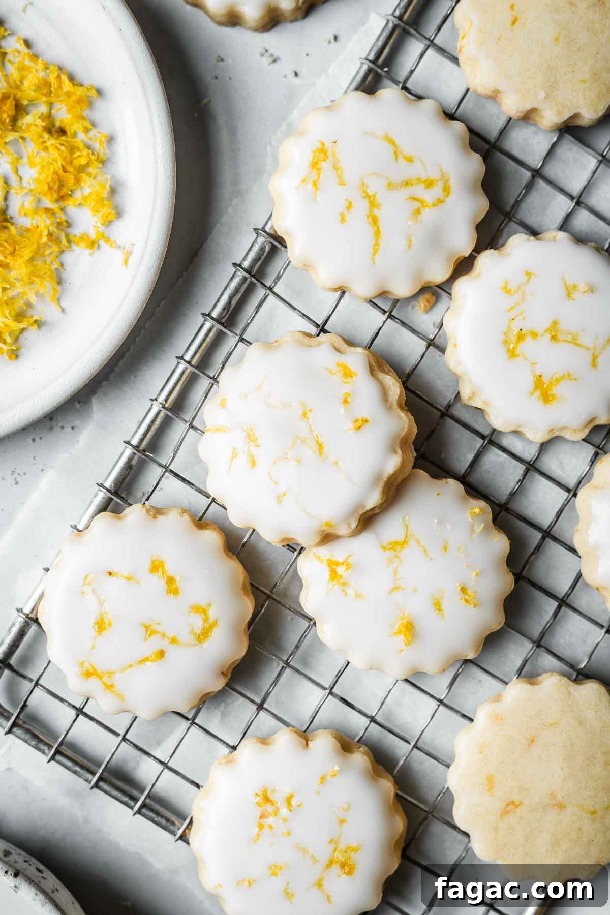 Glazed cookies with lemon zest on a cooling rack.