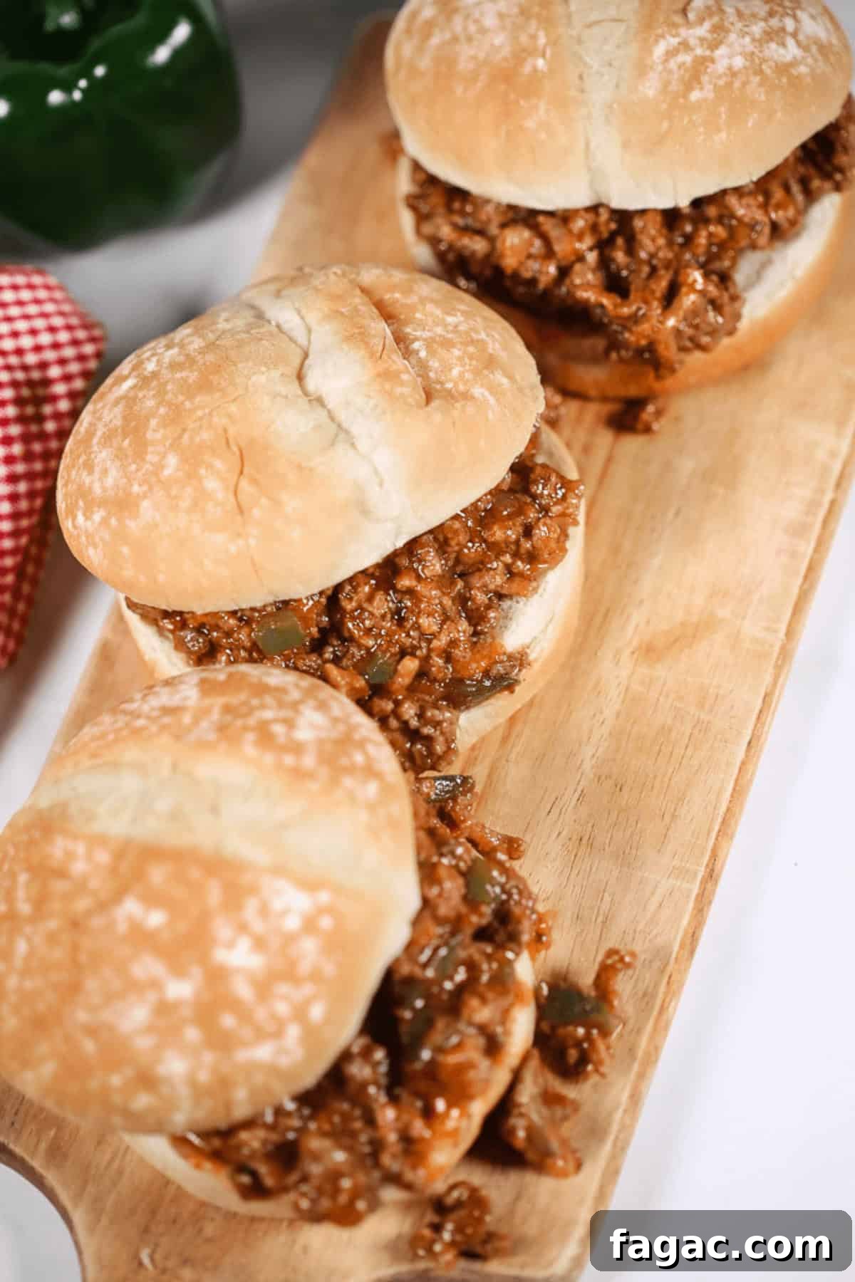 Three Wimpies (Easy Sloppy Joes) with ground meat filling on a wooden cutting board. A red checkered cloth and a green pepper are visible in the background.