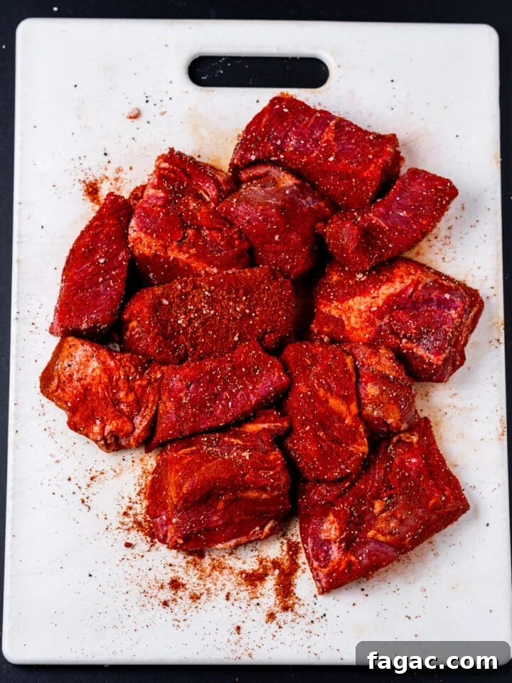 white cutting board with large chunks of raw, seasoned beef chuck roast
