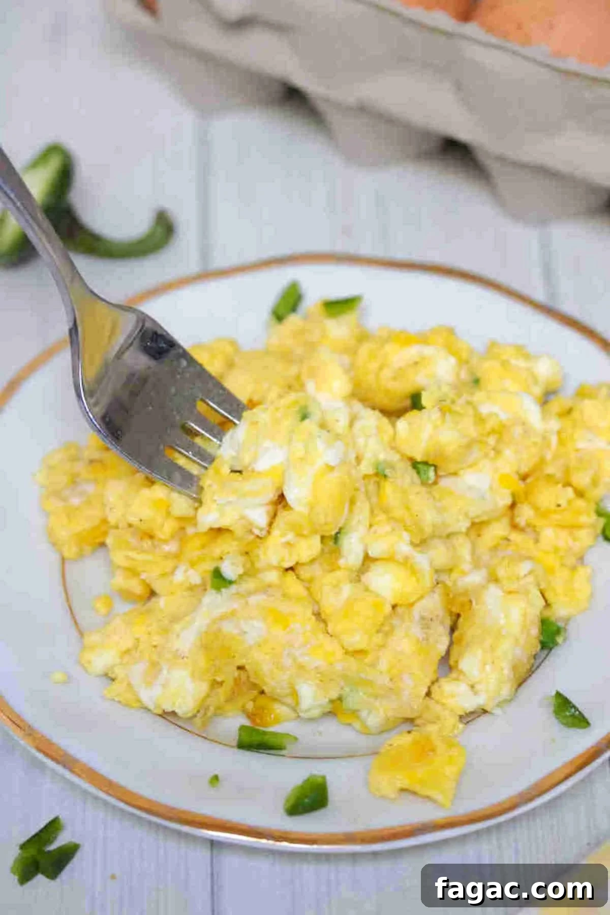 Scrambled eggs without milk on a white plate with a fork in them and topped with jalapenos.
