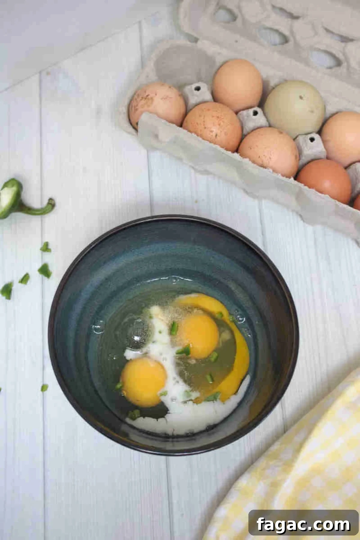 Two eggs in a bowl with milk and jalapeno.