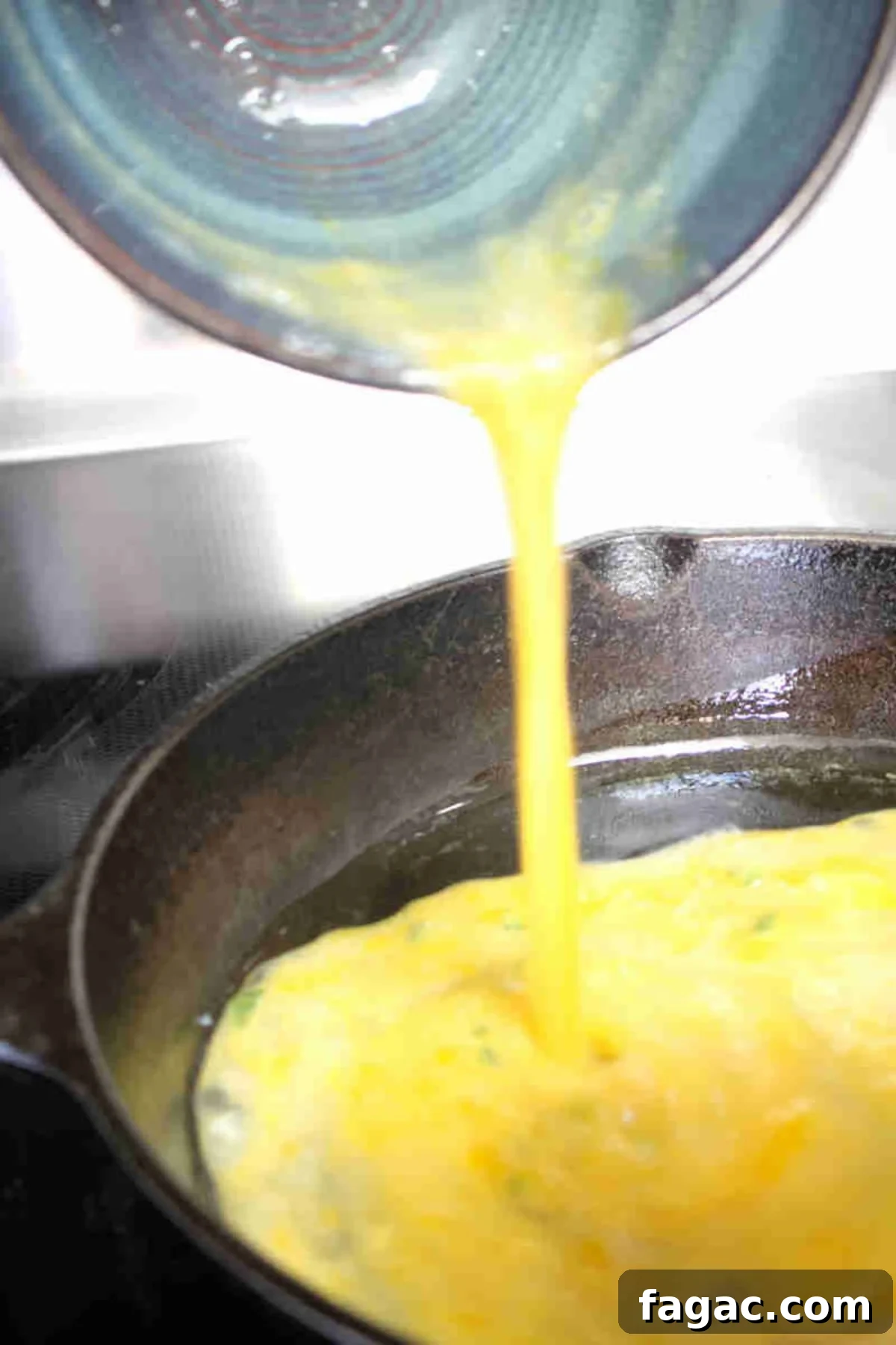 Scrambled eggs being poured into a cast iron pan.