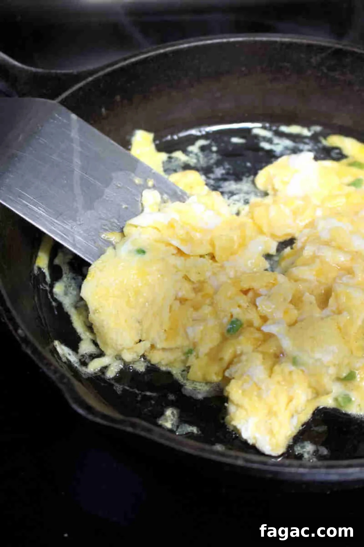 Scrambled eggs in a cast iron pan with a metal spatula.
