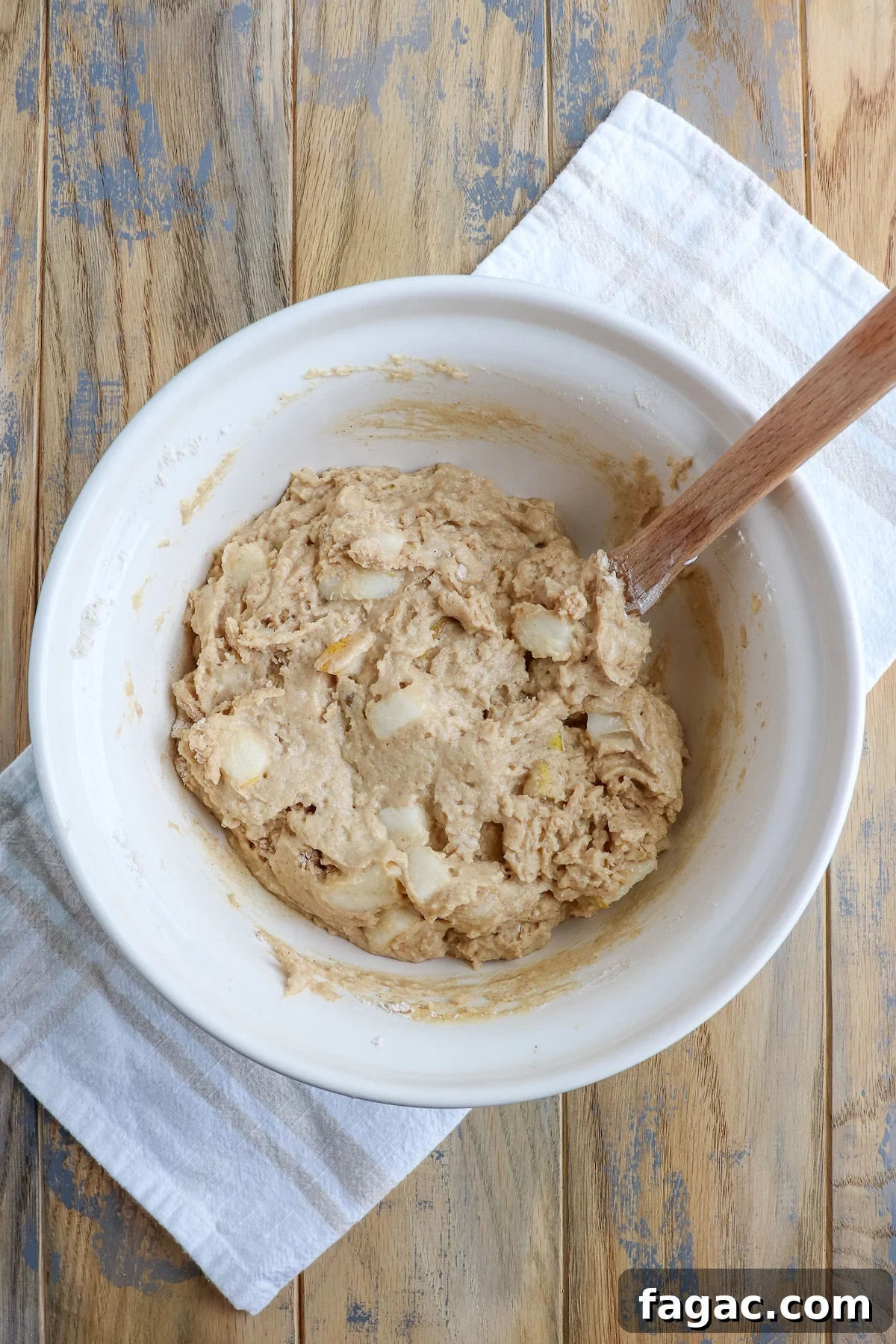 Stirring the thick muffin batter with visible pear chunks in a ceramic mixing bowl. 