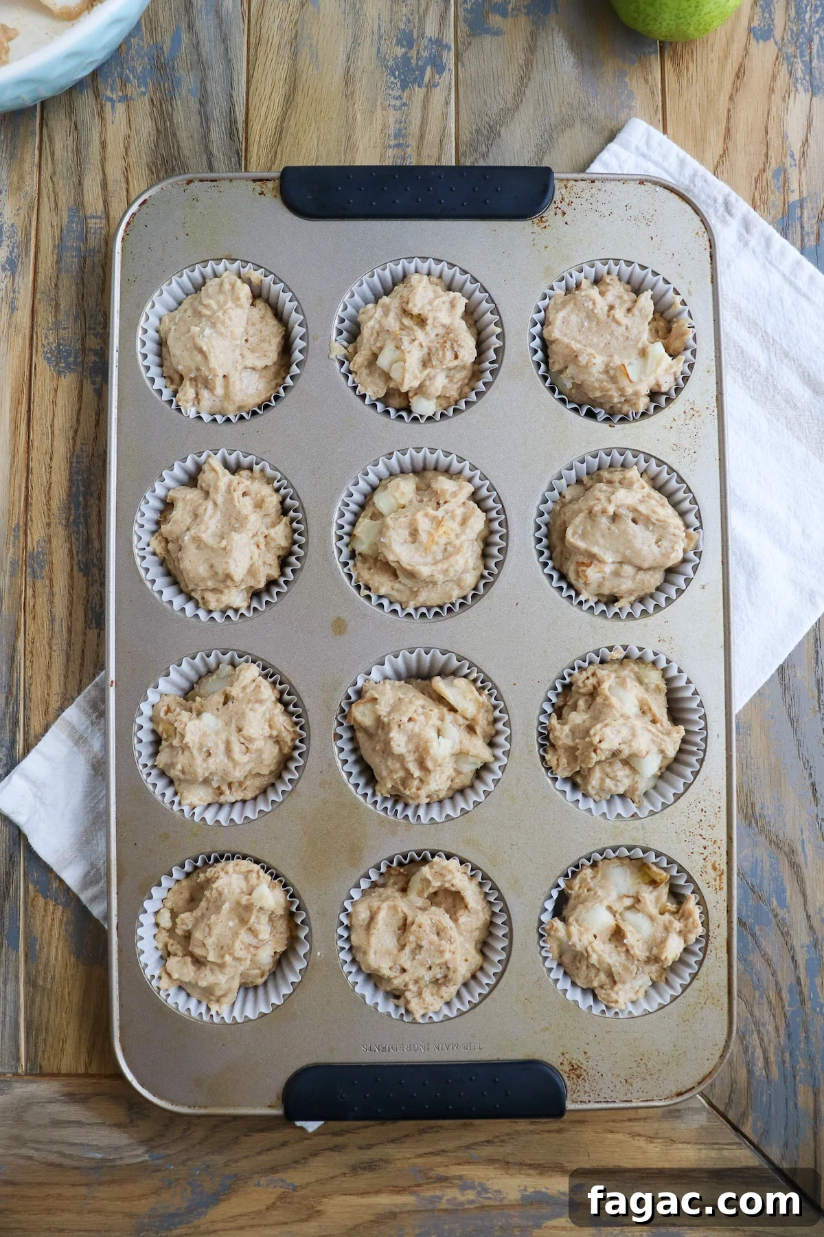 Pear muffin batter in lined muffin pan just before baking, visible chunks of juicy pear in this tasty pear recipe. 