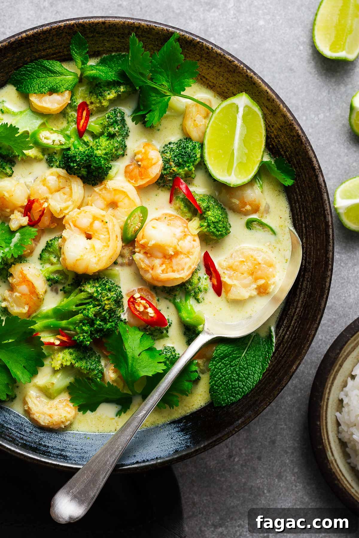 Thai Red Curry Paste Substitutes: What to Use and What to Avoid 11 A ceramic bowl with Thai green curry with shrimp and broccoli garnished with fresh herbs and lime wedges with a serving spoon.