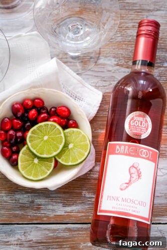 A bottle of pink moscato wine next to a bowl of cranberries and sliced limes.